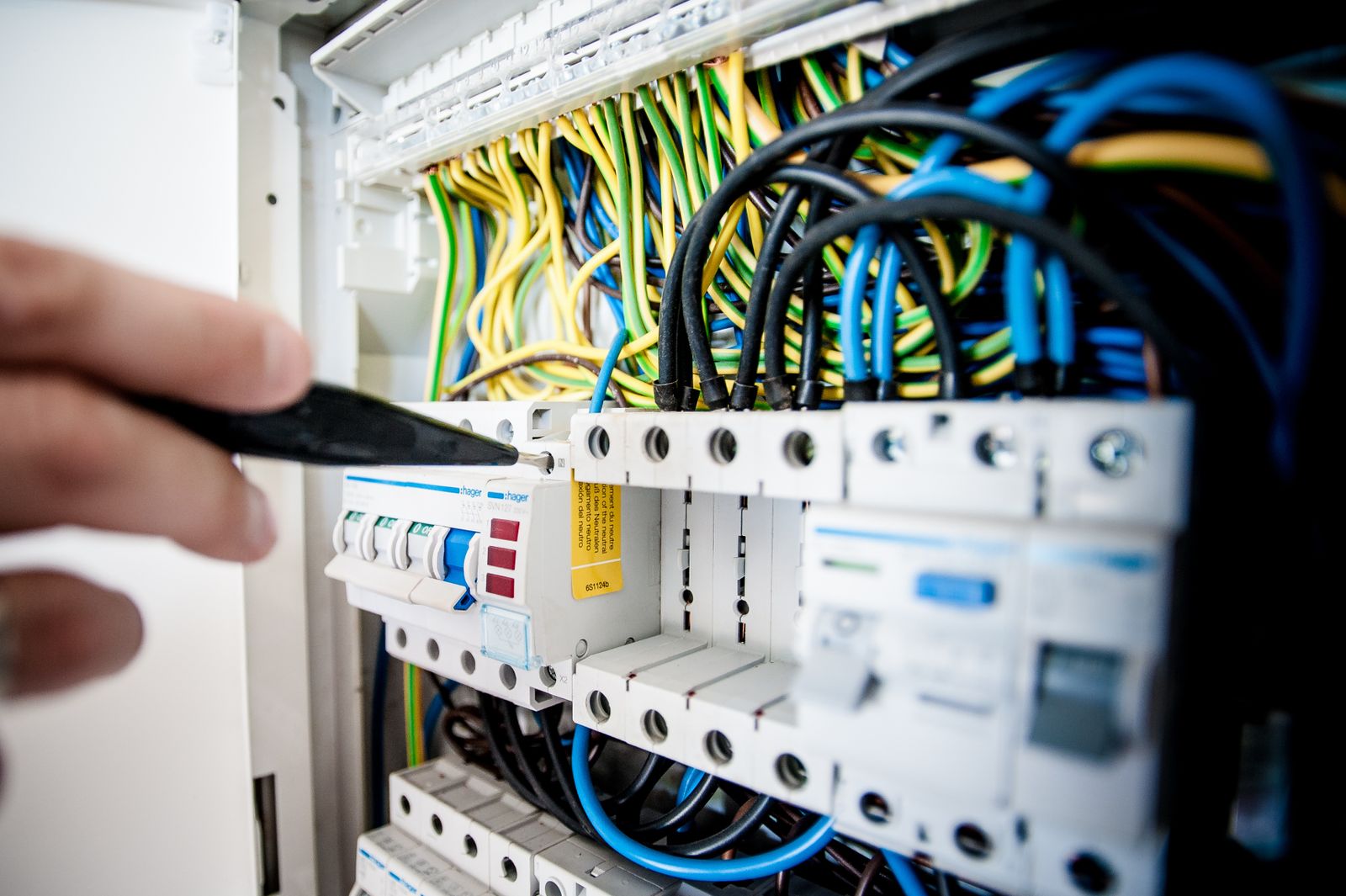 A licensed electrician's hands working inside a modern residential breaker panel